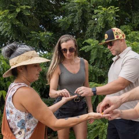 People exchanging small items outdoors, surrounded by lush green foliage.