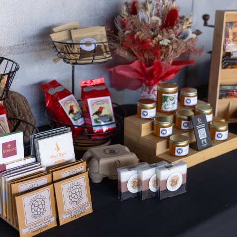 Display of assorted packaged foods and jars on a black tablecloth with a floral arrangement.