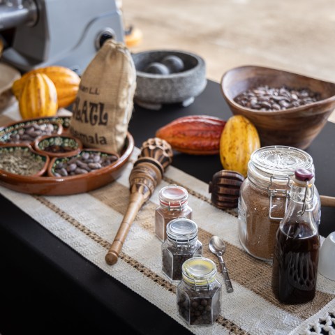 Table with cocoa pods, jars of ingredients, and kitchen utensils.