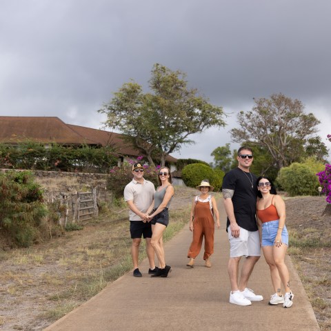 Five people posing on a path with trees and a house in the background.