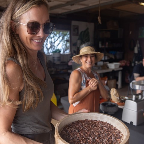 Woman in sunglasses holding a bowl of cocoa nibs, with another person smiling in the background.