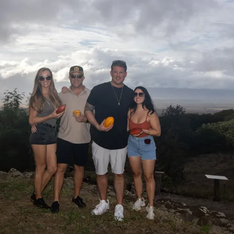 Four people posing with cocoa pods in a scenic outdoor setting.