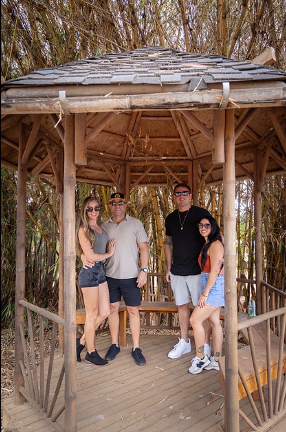 Four people stand in a wooden gazebo surrounded by bamboo.